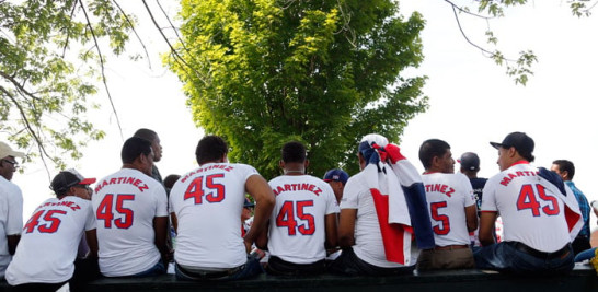 Fanáticos de Pedro Martínez aparecen sentados en una cerca en el lugar donde se realiza la ceremonia de exaltación de Martínez al Salón de la Fama del béisbol el domingo, 26 de julio de 2015, en Cooperstown, Nueva York. (AP Photo/Mike Groll)