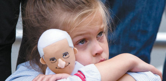 Espera. Una niña sostiene un muñeco con la figura del líder de la iglesia Católica mientras espera su paso por una calle de Filadelfia.