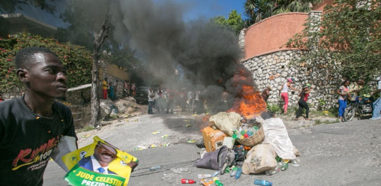 Protestas. Un haitiano corre con una promoción del candidato Jude Célestin cerca de una barricada incendiada durante las  en Haití luego de conocerse los resultados electorales de la primera vuelta.