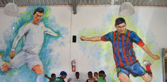 Junior,  Andy,  Javier,  Juan Francisco,  Nervi, William y Jonathan posan en el mural del comedor: dos figuras gigantes de los futbolistas Cristiano Ronaldo y Lionel Messi.