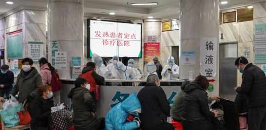 La gente espera mientras el personal médico usa ropa protectora, en el Hospital de la Cruz Roja de Wuhan. /AFP