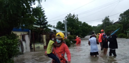Un miembro de la Denfensa Civil de RD traslada en sus brazos a una niña mientras cruza por las inundaciones de una calle en la provincia de Hato Mayor.