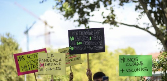 Manifestantes sostienen pancartas que dicen "Más hospitales, menos soldados" y "Menos sacerdotes, más vacunas" durante la protesta. Foto: Oscar del Pozo/AFP.