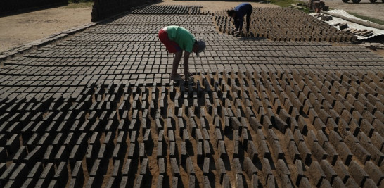 Cristian, al centro, voltea ladrillos de arcilla para que el sol los seque antes de que sean puestos en un horno en una pequeña fábrica en Tobati, Paraguay. Foto: AP/Jorge Sáenz.