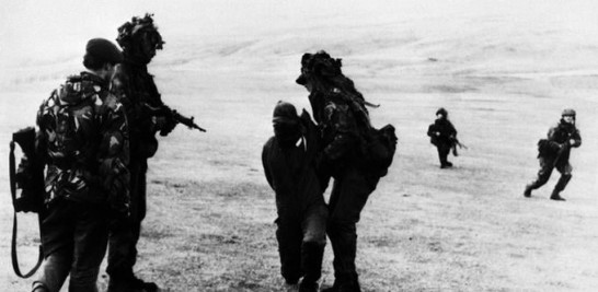 Tres Royal Marines toman prisionero a un soldado argentino. Le cubren los ojos por seguridad durante el avance británico hacia Puerto Argentino (AP)
