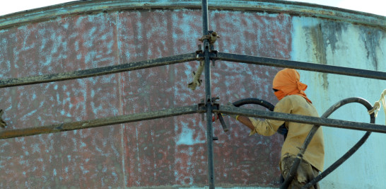 Hombre retirando la pintura al tanque de agua como parte del mantenimiento. Foto: Leonel Matos/LD.