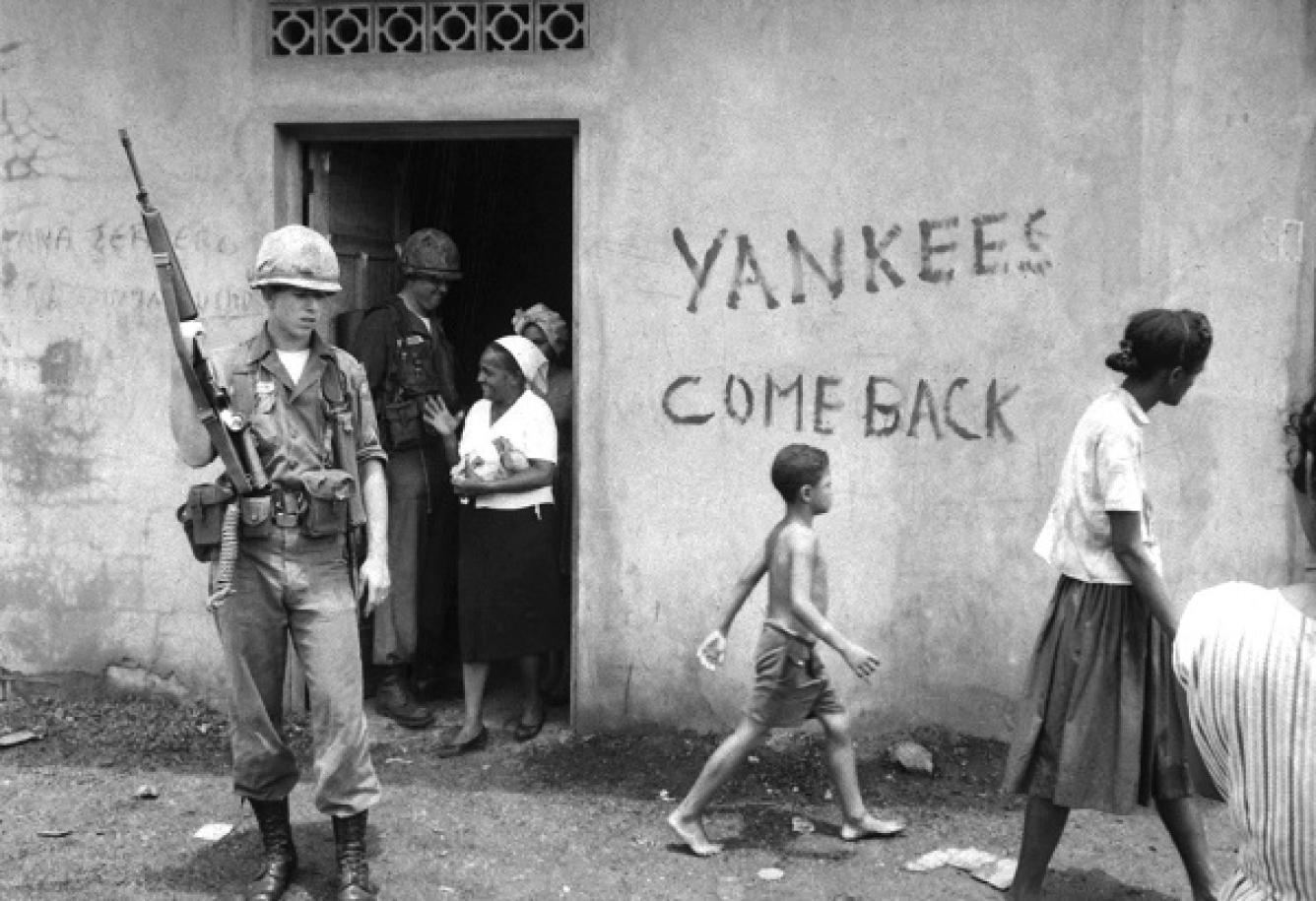 Un soldado vigila la entrada cuando una mujer dominicana sale de un centro de distribución de alimentos en Santo Domingo, RD