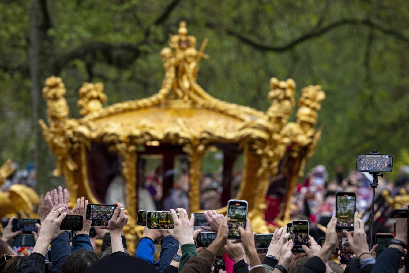 La gente usa sus teléfonos móviles mientras el rey Carlos III y la reina Camila de Gran Bretaña viajan en el Gold State Coach, regresando de la ceremonia de coronación, en Londres, el sábado 6 de mayo de 2023.