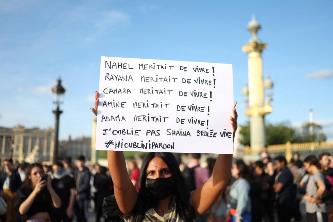 Un manifestante sostiene un cartel con los nombres de las víctimas con la cita 