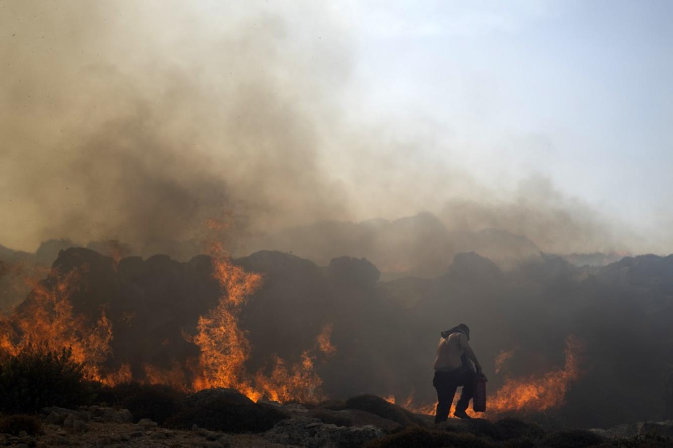 Un hombre intenta extinguir un incendio, cerca de la localidad costera de Lindos, en la isla de Roda
