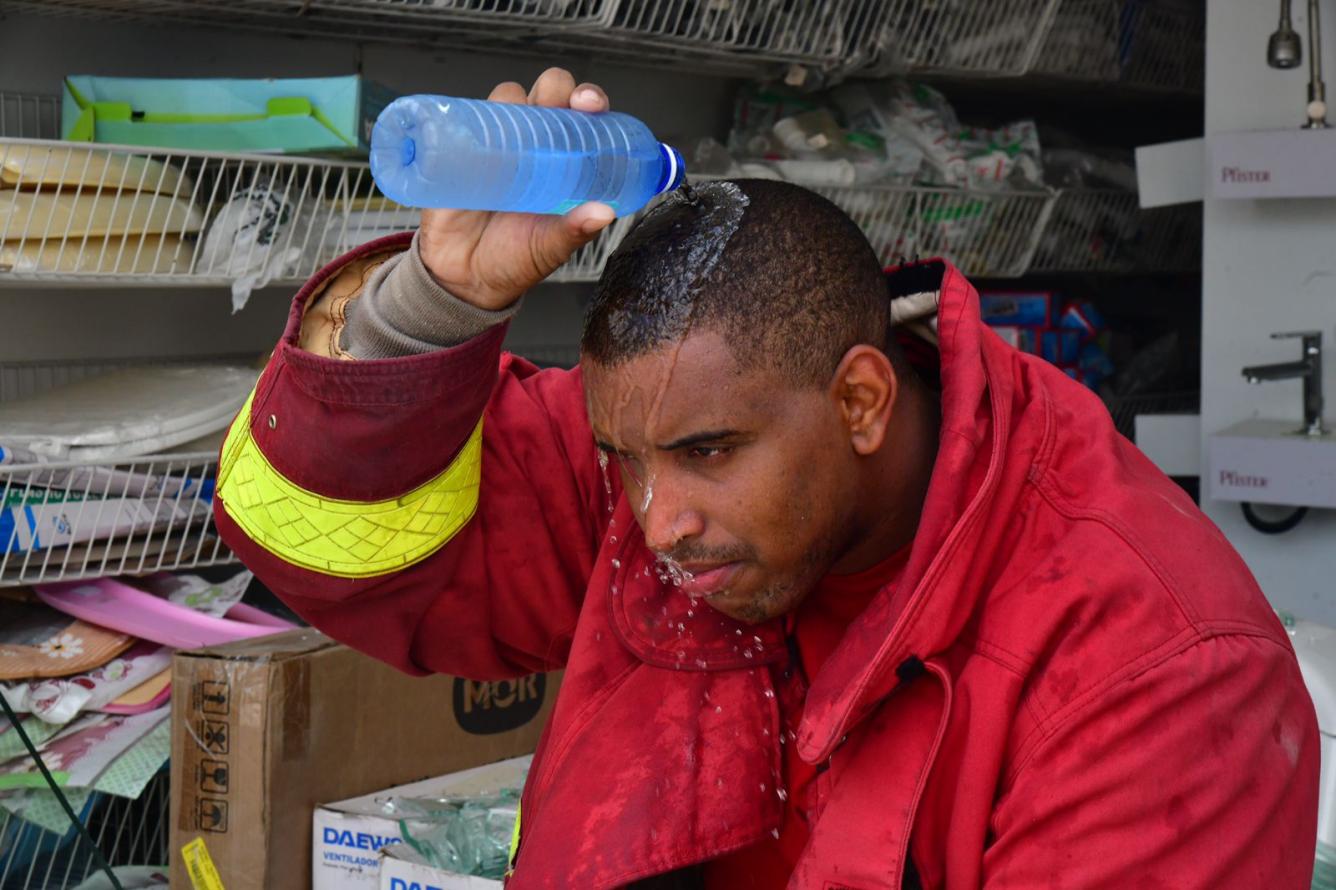 Un bombero se derrama el agua de una botella en su cabeza para refrescarse.