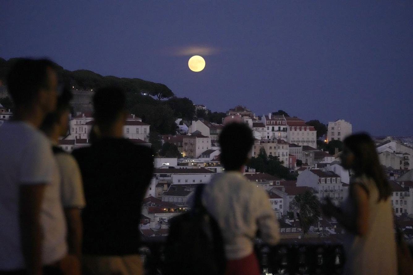 La gente observa una superluna elevarse sobre Lisboa