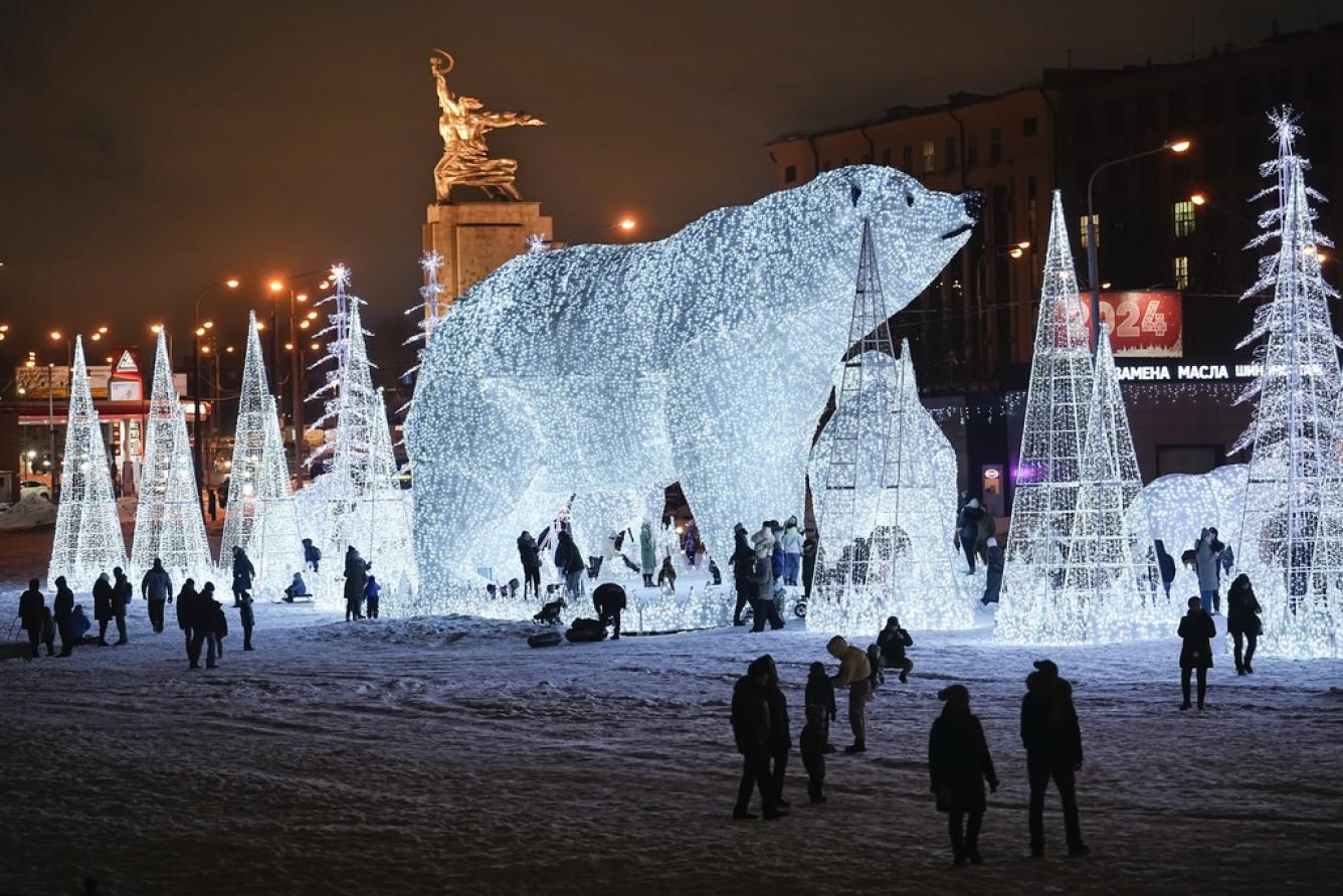 La gente camina y juega en un parque decorado para las festividades de Año Nuevo y Navidad con la escultura de la Mujer Trabajadora y Kolkhoz (granja colectiva), hecha de acero inoxidable por la famosa escultora soviética Vera Mukhina, en el centro izquierda, al fondo en Moscú, Rusia, el domingo. , 24 de diciembre de 2023. (Foto AP/Alexander Zemlianichenko)