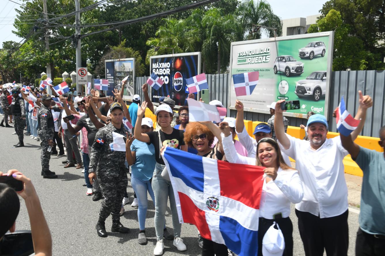 Personas en las diferentes calles portan banderas y saludan al presidente Luis Abinader y Raquel Peña mientras se dirigen al Teatro Nacional.