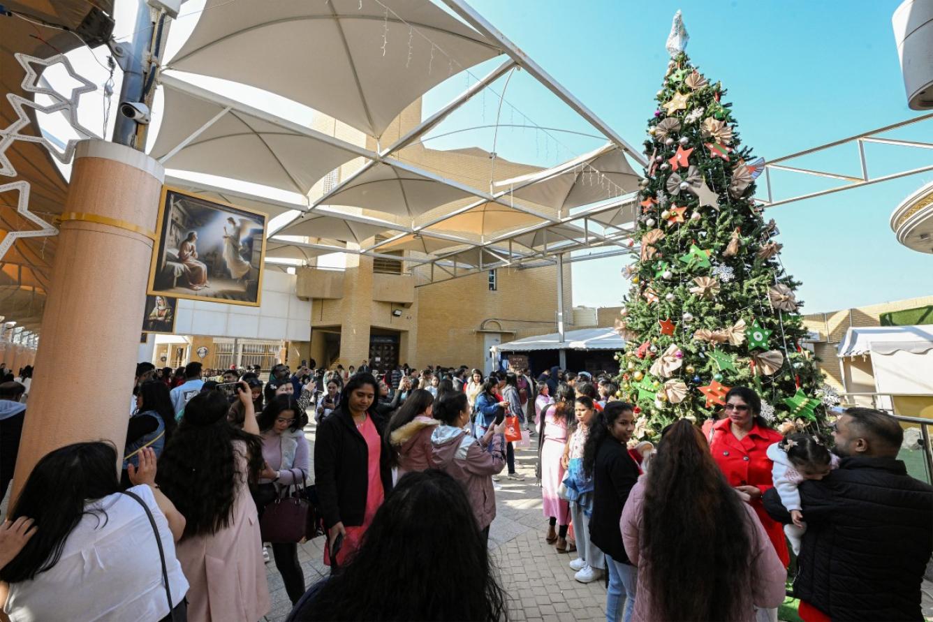 La gente posa junto a un árbol de Navidad gigante en la Concatedral Católica de la Sagrada Familia en la ciudad de Kuwait el 25 de diciembre de 2024.