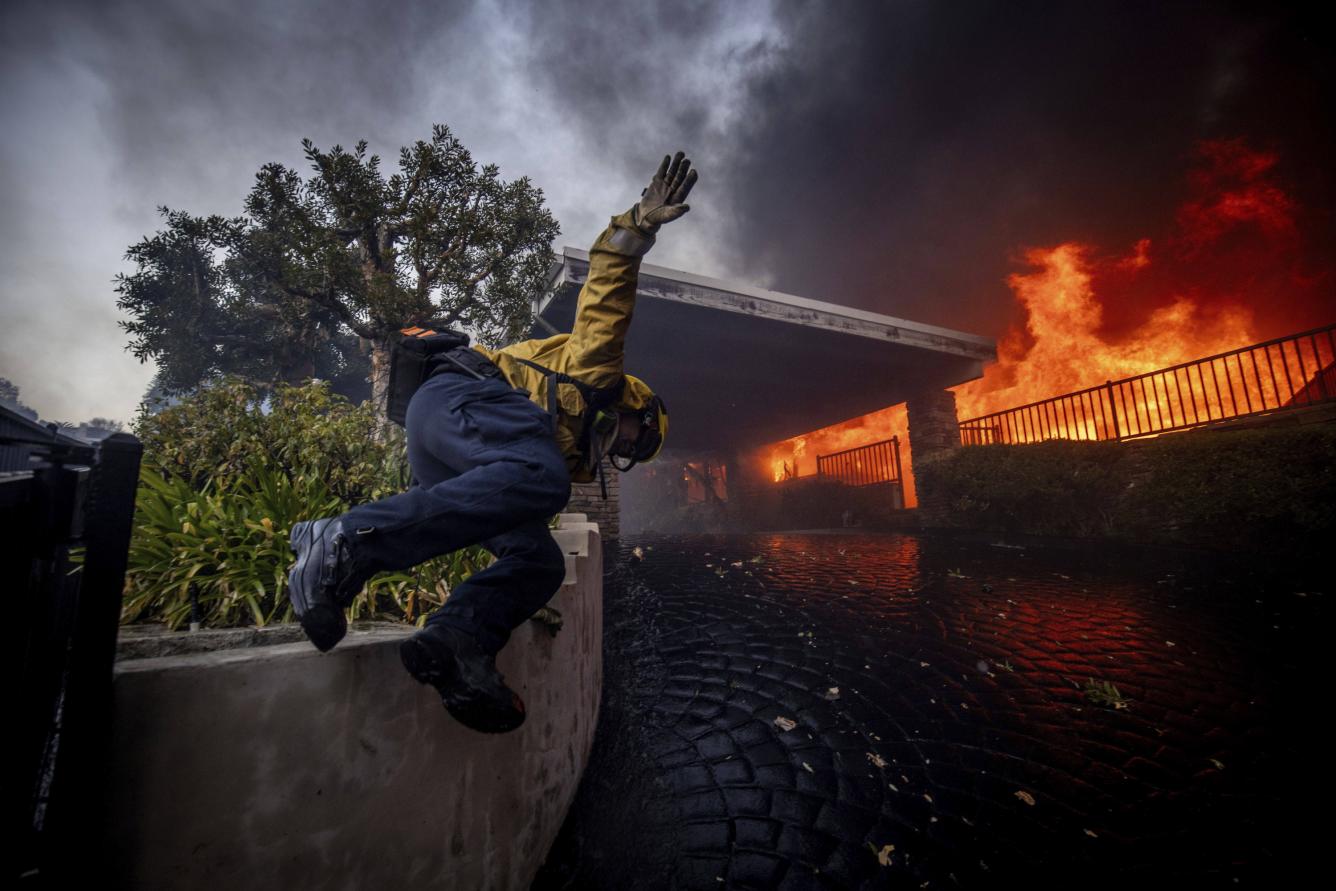 Un bombero salta una valla mientras combate el incendio de Palisades