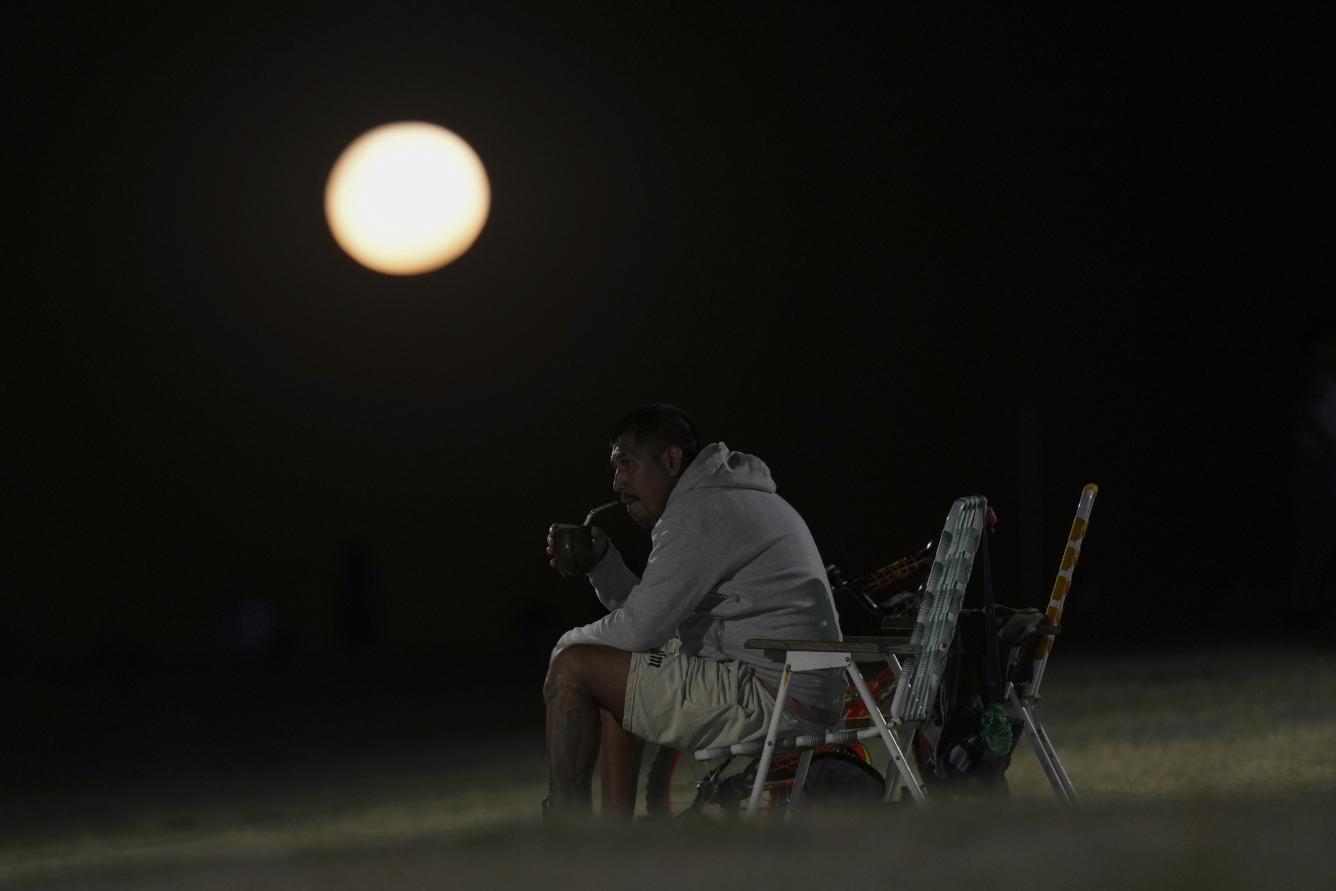 Un hombre toma mate con la luna en forma de lobo de fondo en Buenos Aires