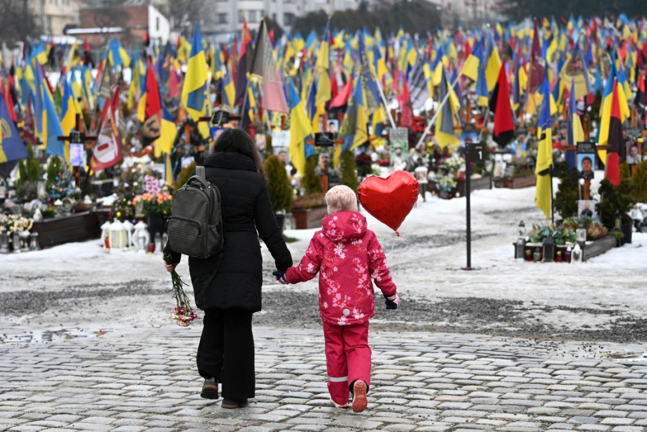 Una madre y su hija caminan con un globo en forma de corazón el Día de San Valentín en el Cementerio Militar de Lychakiv, en Lviv, el 14 de febrero de 2026, durante la invasión rusa de Ucrania. (Foto de YURIY DYACHYSHYN / AFP)