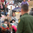 Las mujeres sostienen sus pulseras en alto con la esperanza de que los agentes de la Patrulla Fronteriza de EE. UU. las elijan para ser procesadas después de esperar días entre dos muros fronterizos para solicitar asilo.