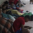 Migrantes venezolanos sentados junto a la pared de un edificio mientras se resguardan de la lluvia, en Matamoros, México, el sábado 13 de mayo de 2023.