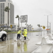 los trabajadores aseguran un letrero mientras soplan fuertes vientos de la tormenta tropical Harold