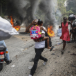 Varias personas corren junto a neumáticos en llamas durante una protesta contra el primer ministro Ariel Henry, el lunes 5 de febrero de 2024, en Puerto Príncipe, Haití.