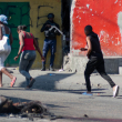 Varias personas caminan junto a cadáveres quemados y un agente de policía armado que vigila una calle tras otra jornada violencia de bandas el 21 de marzo de 2024, en Puerto Príncipe, Haití