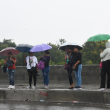 Varias personas se cubren de la lluvia con paraguas mientras esperan el transporte público.