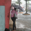 Una mujer se cubre de la lluvia mientras camina por una acera inundada de la capital.