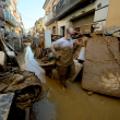 A man with a mask drags a wheelbarrow among mud and debris in a street of Paiporta, south of Valencia, eastern Spain, on November 6, 2024, in the aftermath of deadly floods. - Spain announced an aid package worth 10.6 billion euros ($11.5 billion) to rebuild regions devastated by its worst floods in a generation that have killed 219 people. (Photo by JOSE JORDAN / AFP)