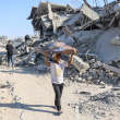 Un niño palestino con sus pertenencias camina entre los escombros de los edificios destruidos en el barrio de Al-Tuffah, en la ciudad de Gaza, el 27 de octubre de 2025. (Foto de Omar AL-QATTAA / AFP)