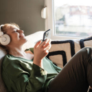 Mujer joven relajándose en un sofá y escuchando música en su teléfono a través de auriculares.