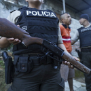 Un agente de policía hace guardia mientras una persona es detenida durante un registro en busca de armas o drogas, dentro de una operación para luchar contra las bandas criminales, en el vecindario de Nueva Guayaquil, en Guayaquil, Ecuador, el 4 de abril de 2024.