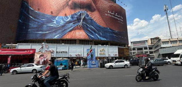 Vehículos circulan junto a una valla publicitaria con una imagen del estrecho de Ormuz y los labios cosidos del presidente estadounidense Donald Trump, en una plaza del centro de Teherán, Irán, el sábado 2 de mayo de 2026.