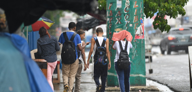 Estudiantes caminan bajo la lluvia en una acera del Distrito Nacional.