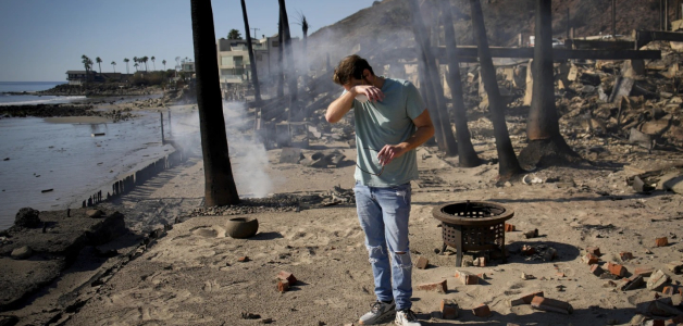 Luke Dexter reacciona mientras examina los restos de la  propiedad frente a la playa de su padre, devastada por el fuego.