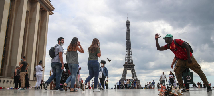 Un vendedor de souvenirs de la Torre Eiffel explica cómo tomarse una foto con la Torre Eiffel a una mujer, en la plaza Trocadero en París, Francia, el 14 de agosto de 2020.