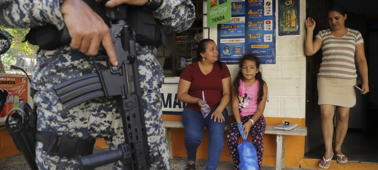 Varias personas se sientan ayer en la entrada de una tienda custodiada por un militar en San Antonio Los Ranchos, El Salvador.
