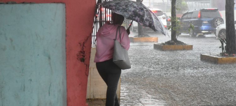 Una mujer se cubre de la lluvia mientras camina por una acera inundada de la capital.