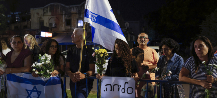 Personas portan flores y banderas israelíes a la llegada de vehículos que transportan los cuerpos de cuatro rehenes entregados tras un acuerdo de alto el fuego e intercambio de prisioneros entre Israel y facciones palestinas en Gaza, frente al Centro Nacional de Medicina Forense en Tel Aviv el 13 de octubre de 2025.