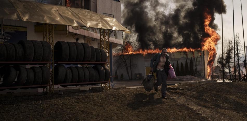 Un hombre corre con artículos recuperados de una tienda en llamas luego de un ataque ruso, el 25 de marzo de 2022, en Járkiv, Ucrania.