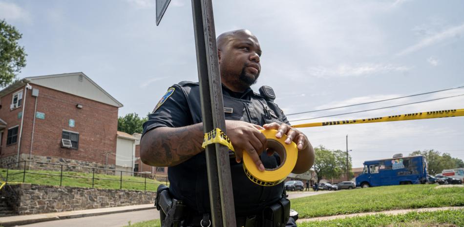 Un oficial de policía de Baltimore cuelga una cinta policial en el lugar de un tiroteo masivo en el vecindario de Brooklyn Homes el 2 de julio de 2023 en Baltimore, Maryland.