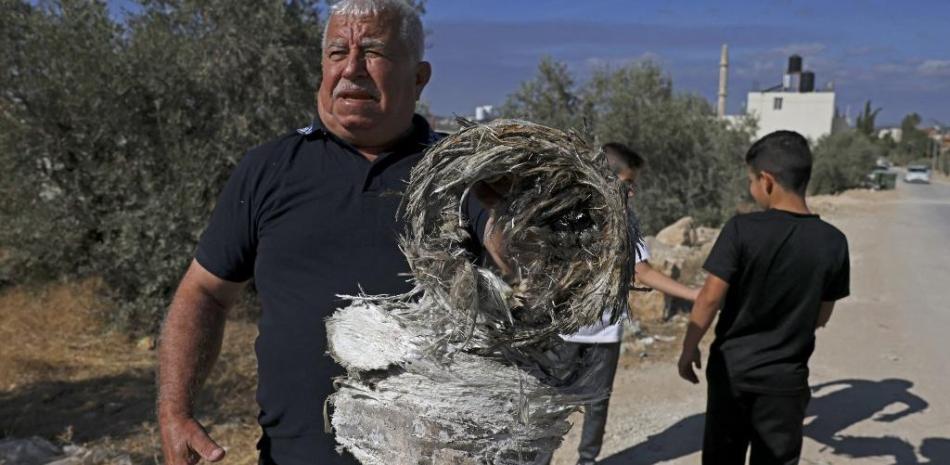 Un residente sostiene los restos de un cohete que cayó en la aldea de Kharas, al norte de la ciudad de Hebrón, en Cisjordania, el 7 de octubre
