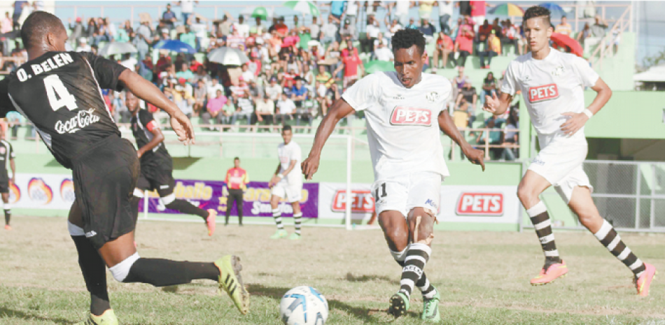 El nacional haitiano Ronald Pierre conduce el balón ante la mirada de un jugador del Bauger FC, durante un partido realizado en el estadio Bragañita García, de la ciudad de Moca, correspondiente a la Liga Dominicana de Fútbol.