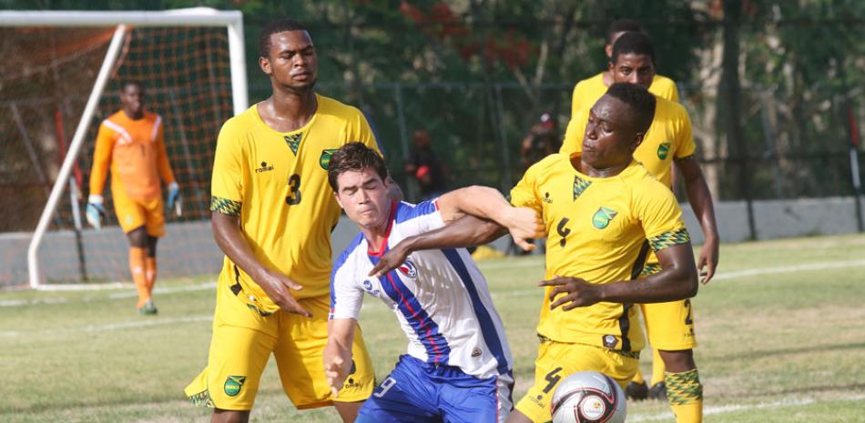 Un jugador de República Dominicana hace esfuerzos por alcanzar el balón que es protegido por un jugador de Jamaica.