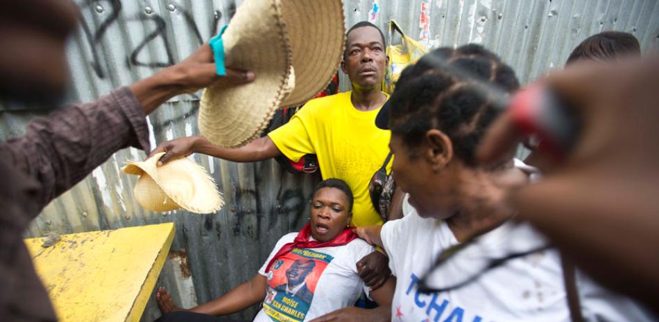 Manifestantes ayudan a una mujer luego de que le lanzaran gas lacrimógeno durante una protesta ante el consejo electoral en Puerto Príncipe, Haití, el sábado 12 de diciembre de 2015.