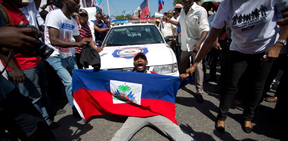 En esta fotografía de archivo tomada el 21 de julio de 2015, un manifestante haitiano sostiene una bandera, mientras grita consignas contra el racismo y bloquea un carro de policía, durante una marcha al frente de la oficina del Primer Ministro de Haití en protesta por la deportación de haitianos de República Dominicana, en Port-au-Prince, Haití.