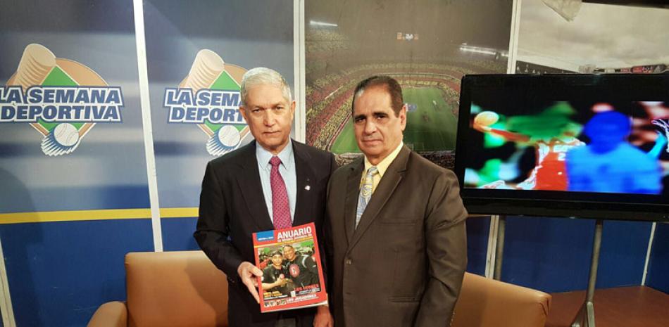 El licenciado Juan Puello recibe un libro Anuario de Beisbol Invernal de manos de su editor periodista Héctor J. Cruz, productor general de La Semana Deportiva.