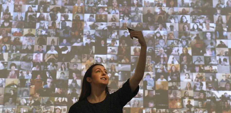 Una mujer posa para un selfi ante una pantalla con miles de imágenes de personas en las redes sociales durante la presentación de la exposición que muestra el selfi como un arte en la Galería Saatchi en Londres (Reino Unido) hoy, 30 de marzo de 2017. (EFE/Andy Rain)