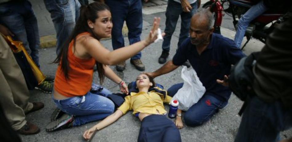 En esta imagen del 20 de abril de 2017, una mujer es asistida por otros manifestantes tras caerse por el efecto de los gases lacrimógenos durante protestas contra el gobierno en Caracas, Venezuela.